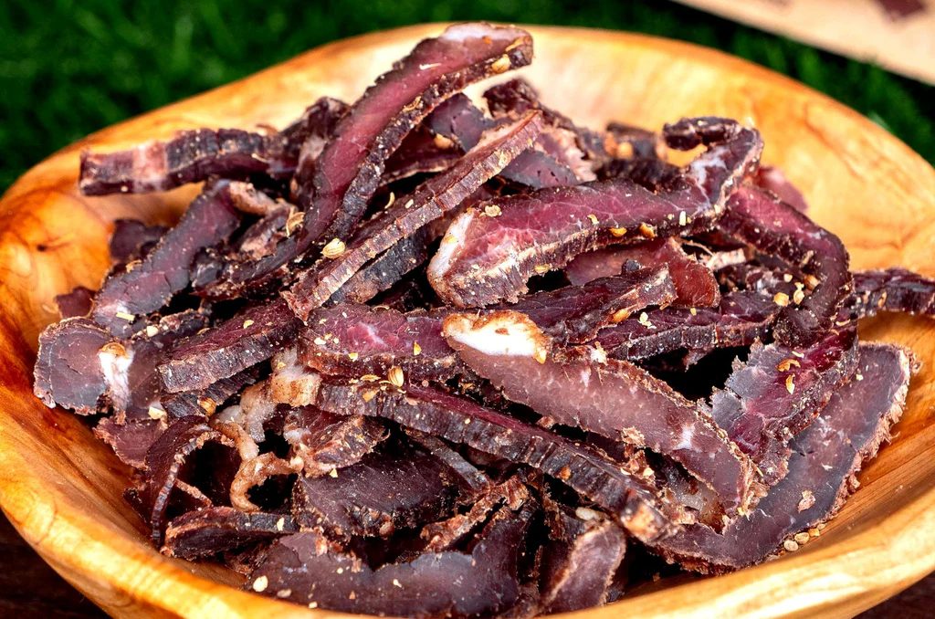A wooden bowl filled with thinly sliced biltong, showing its dark, cured texture with visible spices and seasonings
