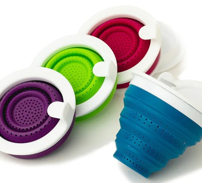 A set of four collapsible silicone tea infusers in purple, green, pink, and blue. Each infuser has a white rim and small perforations for steeping loose-leaf tea, designed for easy use and storage