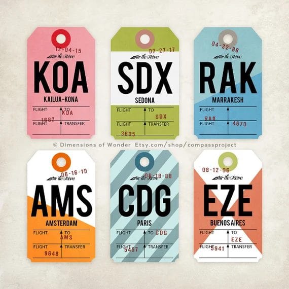 A collection of six vintage-style luggage tags displaying airport codes: KOA (Kailua-Kona), SDX (Sedona), RAK (Marrakesh), AMS (Amsterdam), CDG (Paris), and EZE (Buenos Aires), each with unique colors and travel details.