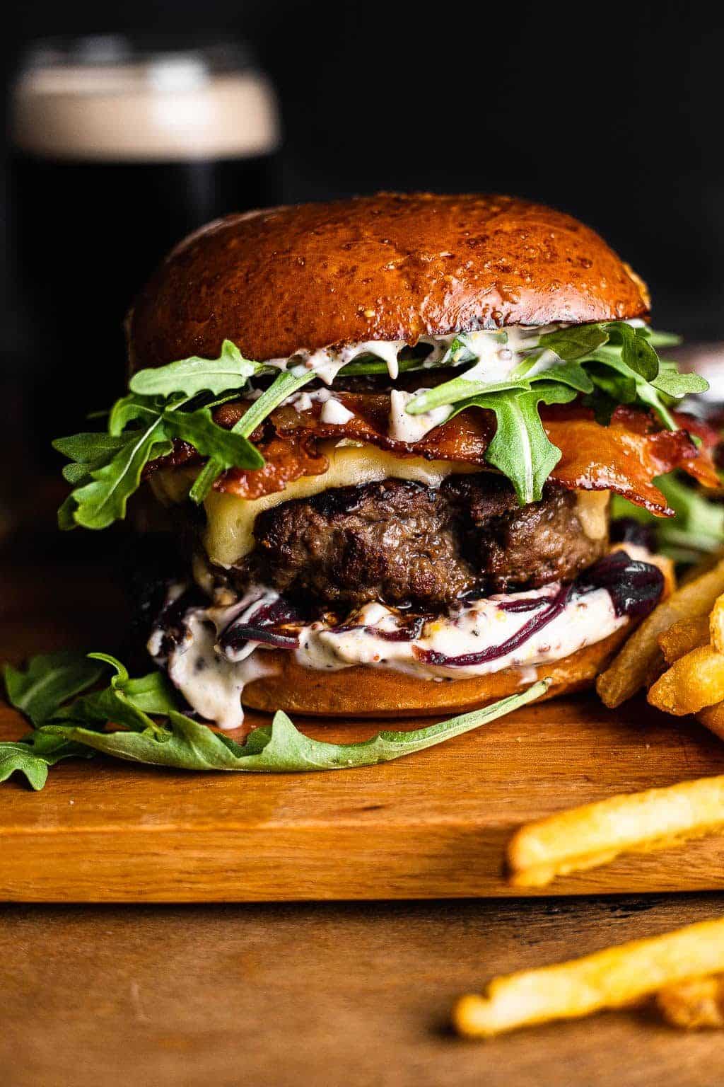  Close-up of a gourmet bacon cheeseburger featuring a juicy beef patty, melted cheese, crispy bacon, fresh arugula, and creamy garlic aioli on a toasted brioche bun, served with golden fries.