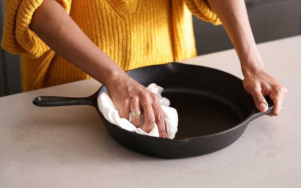 A person wiping a cast iron skillet with a cloth on a kitchen countertop