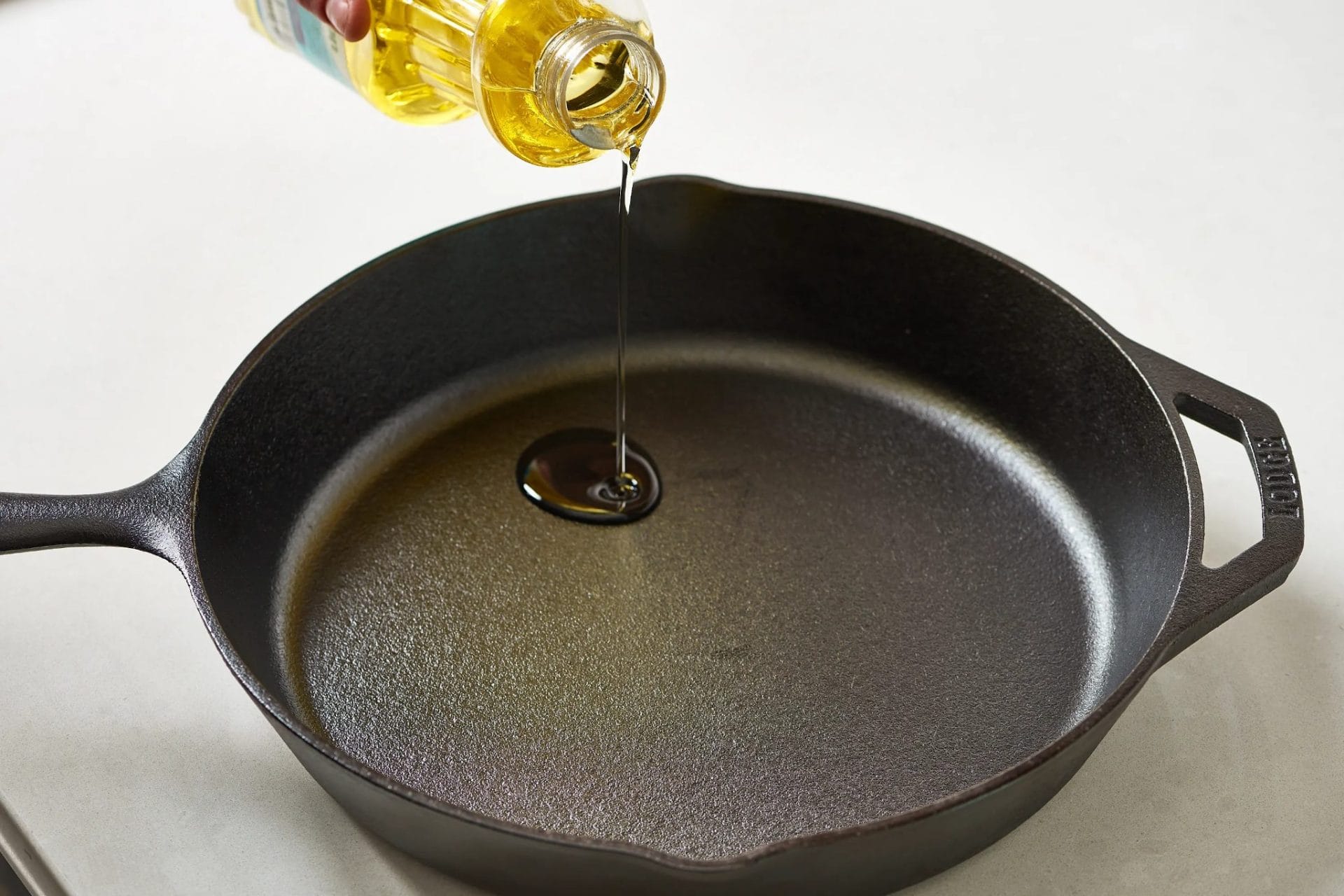 Pouring oil into a cast iron skillet on a kitchen countertop for seasoning