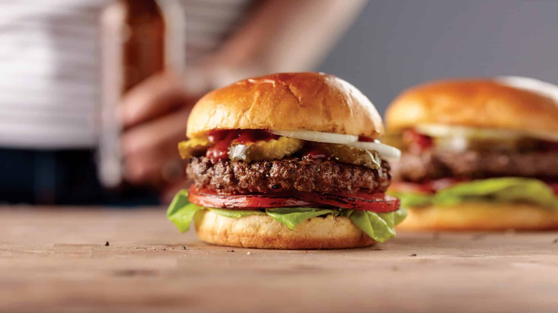  Juicy homemade burger with seasoned ground beef, lettuce, tomato, pickles, and onion on a toasted