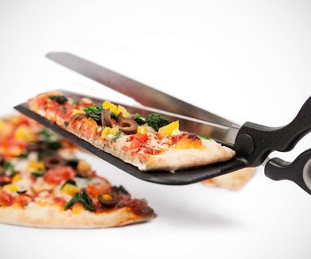 A pair of pizza scissors with an attached spatula cutting and lifting a slice of pizza. This kitchen tool combines scissors for easy slicing and a spatula base to serve the pizza slice without mess.
