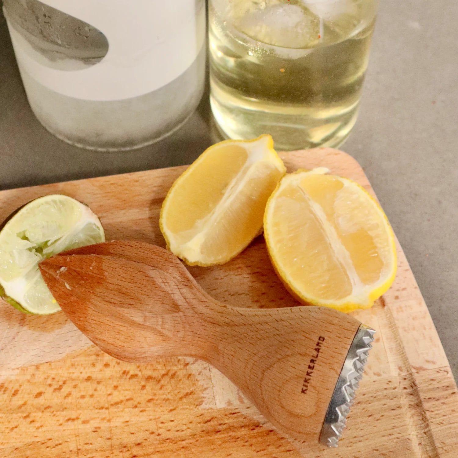 A wooden citrus reamer with a metal muddler end, placed on a wooden cutting board alongside lemon and lime wedges. Ideal for extracting juice and muddling ingredients for cocktails or recipes.