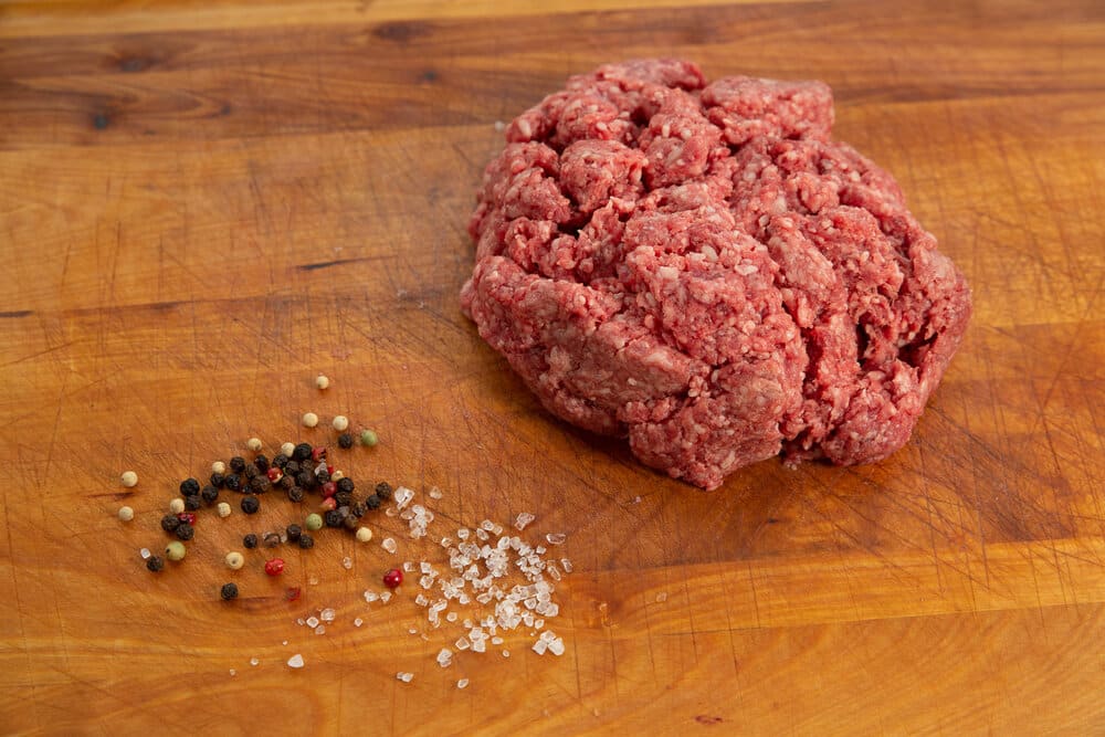 Fresh ground beef with salt and pepper on a wooden cutting board – perfect for seasoning burgers.