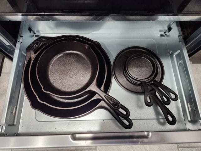 Neatly stacked cast iron skillets of various sizes in a kitchen drawer